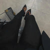 Seated view of black stirrup leggings with pointed heels and a patterned handbag