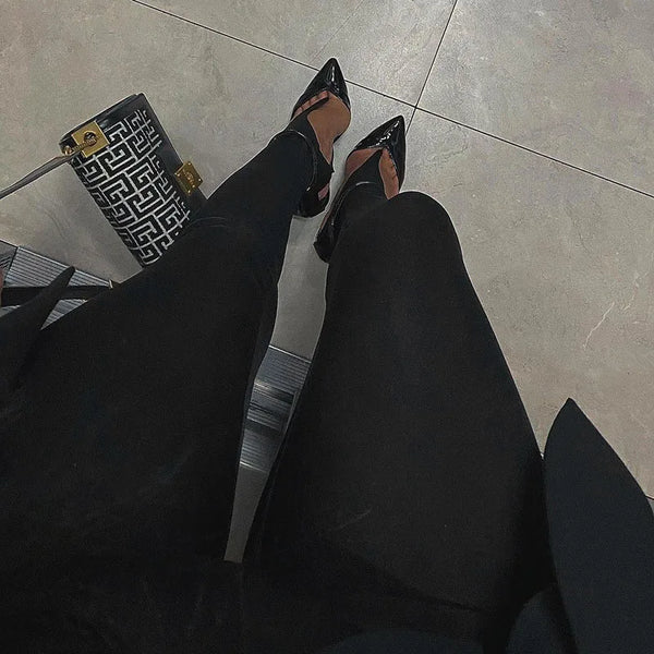Seated view of black stirrup leggings with pointed heels and a patterned handbag
